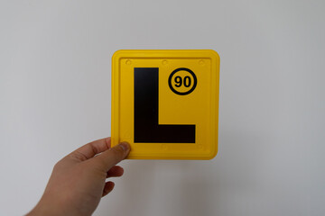 Hand holding a yellow L plate. L plate is learner license in Australian Graduate Licensing System.