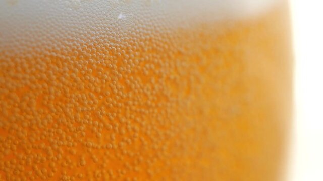 Amazing closeup of a beer glass that is being filled up with more beer. More foam builds, and tiny bubbles race to the top of the glass. Beautiful gradient of gold and amber as backdrop.