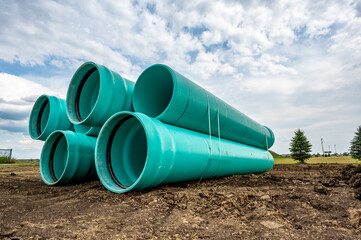 Stacked water main pipe with bell fitting next to an exposed trench for installation