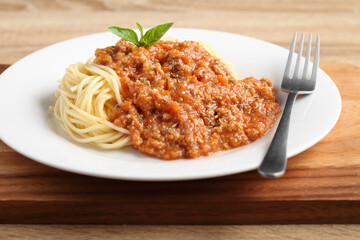 Close up a fork with spaghetti and red sauce in white dish on cutting board