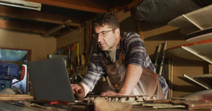Focused caucasian male knife maker in workshop using laptop