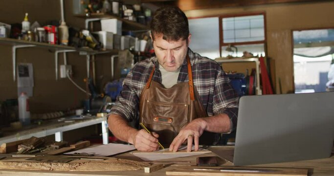 Focused caucasian male knife maker in workshop making drawing
