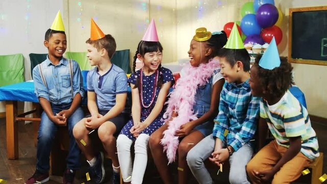 Animation of gold confetti over diverse happy children with hats and balloons having fun at party