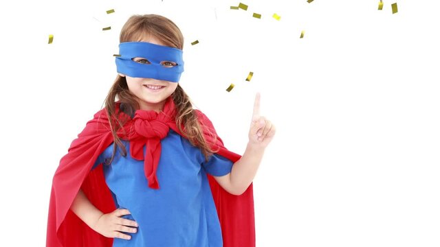 Animation of gold confetti falling over happy girl in superhero party costume waving