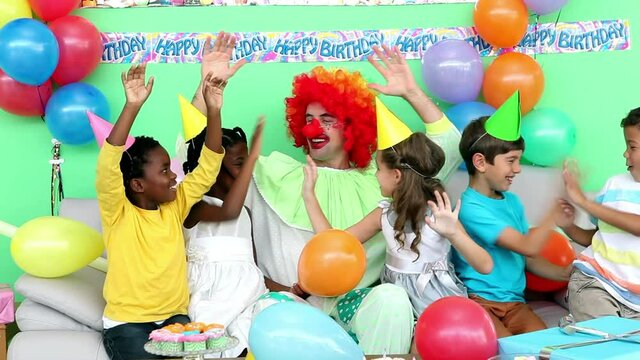 Animation of gold confetti falling over diverse happy children and clown having fun at party