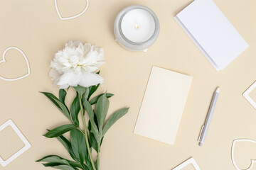 Desktop for romantic holiday with white peony flower, empty paper for writing congratulations, hearts and photo, lit candle