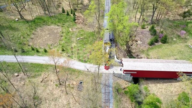 An Aerial View of an 1860's Steam Passenger Train Traveling Thru a Wooded Area as it Passes a Covered Bridge on a Lonely Single Rail Road Track
