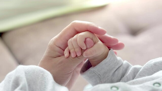 4k Newborn Baby Hand Holding Mother, Mom touching baby tiny hand to make him feeling her love, warm and secure. Maternity, family, birth concept.