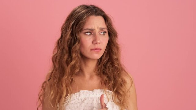 An excited woman fingering her fingers and grabbing her head in a pink studio