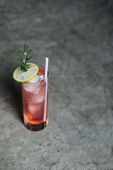 pink cranberry rosemary lime drink cocktail in tall glass against gray background