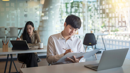 Obraz premium Young Asian businessman holding document and taking notes at the office.
