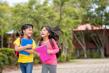 Back to school. Two cute asian child girls with school bag holding book and walk together in the school