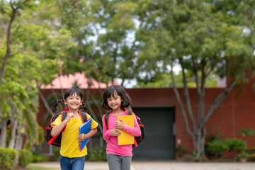 Fototapeta na wymiar Back to school. Two cute asian child girls with school bag holding book and walk together in the school