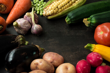 Corn, tomatoes, carrots, potatoes, eggplants, radishes and other vegetables on a black wooden table 