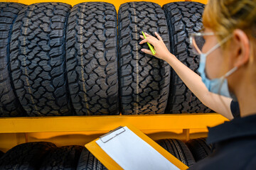 A young woman worker with a clipboard checking stocks of new tires ready to be replaced at a...