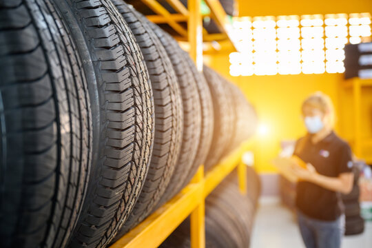 A Young Woman Worker With A Clipboard Checking Stocks Of New Tires Ready To Be Replaced At A Service Center Or Tire Shop. The Background Is A Warehouse. Stock New Tires For The Car Industry.