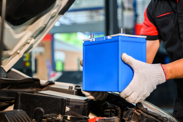 Close-up of a car mechanic in a service center picking up a new battery to replace the car. for...