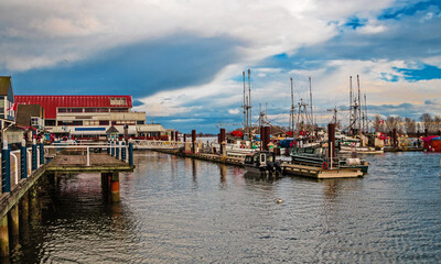 Fototapeta na wymiar Promenade in the village of Steveston, summer grounds of restaurants and fishermen marina at waterfront of Richmond City on a background of stormy sky