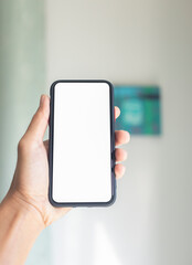 Hand holding black smartphone with white screen mockup and living room background, Mobile phone frameless design concept.	