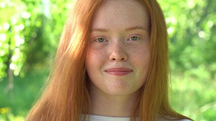 The face of a beautiful red-haired girl in backlight. Portrait a smiling young woman with red hair and freckles against the backdrop of a bright sunny meadow. Natural beauty with freckles
