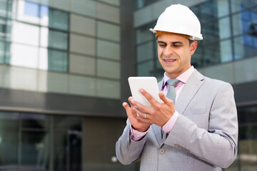 Successful businessman using phone outdoor near large factory