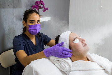 Cosmética masculina. Esteticista Hombre guapo recibiendo tratamiento facial en el spa
