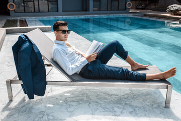 Businessman reading book near swimming pool.