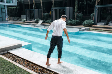 Handsome slender man in business attire prepares to jump into the pool water. Long awaited vacation