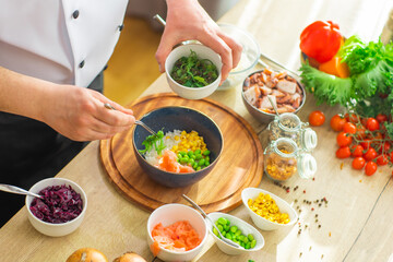 Young prepares a poke bowl in a modern kitchen. The man prepares food at home. Cooking healthy and tasty food.