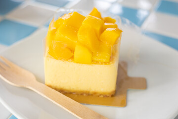 Top view and selective focus of delicious dessert which is cheesecake with mango topping wrapped by clear plastic and served in table in cafe which looks deluxe and elegant sweet menu.
