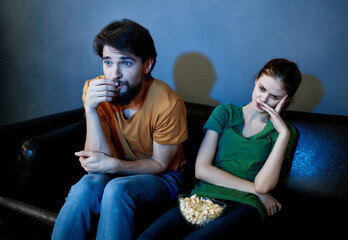 young couple sitting on the couch in the evening watching tv popcorn rest