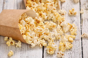 Paper bags with tasty popcorn on light wooden background