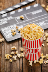 Bucket with tasty popcorn and movie clapper on wooden background, closeup