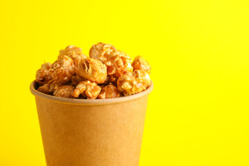 Paper cup with tasty caramel popcorn on color background, closeup