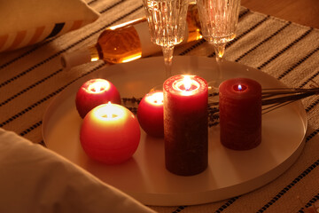 Tray with burning candles and glasses on rug in bedroom