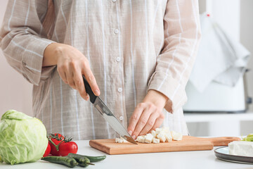 Woman preparing tasty salad with feta cheese in kitchen, closeup