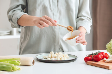 Woman pouring honey onto feta cheese on plate, closeup
