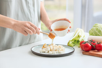 Woman pouring honey onto feta cheese on plate, closeup