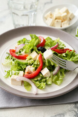 Plate with fresh Greek salad on light background