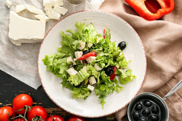 Plate with fresh Greek salad and ingredients on dark wooden background