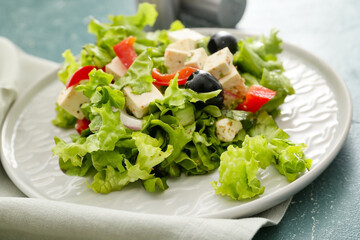 Plate with fresh Greek salad on color background