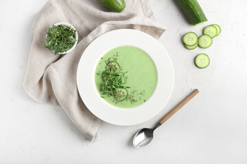 Plate with green gazpacho and ingredients on light background