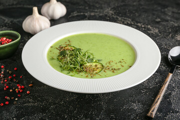 Plate with green gazpacho and spices on dark background