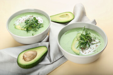 Bowls with green gazpacho and avocado on color background