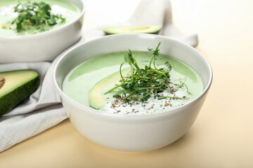 Bowls with green gazpacho and avocado on color background