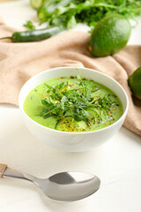 Bowl with green gazpacho and ingredients on light background