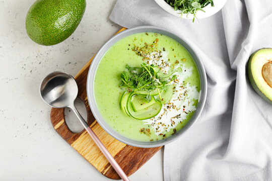 Bowl with green gazpacho and avocado on light background