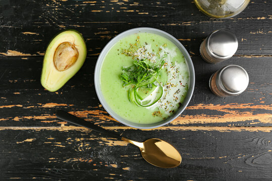 Bowl with green gazpacho, avocado and spices on dark wooden background