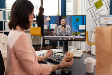 Entrepreneur woman sitting at desk in company office eating sandwich during online videocall...