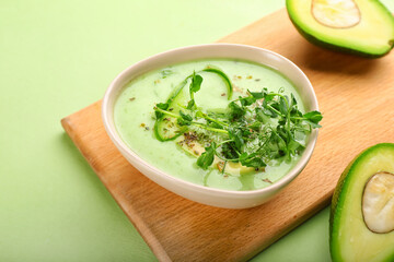 Board with green gazpacho and avocado on color background